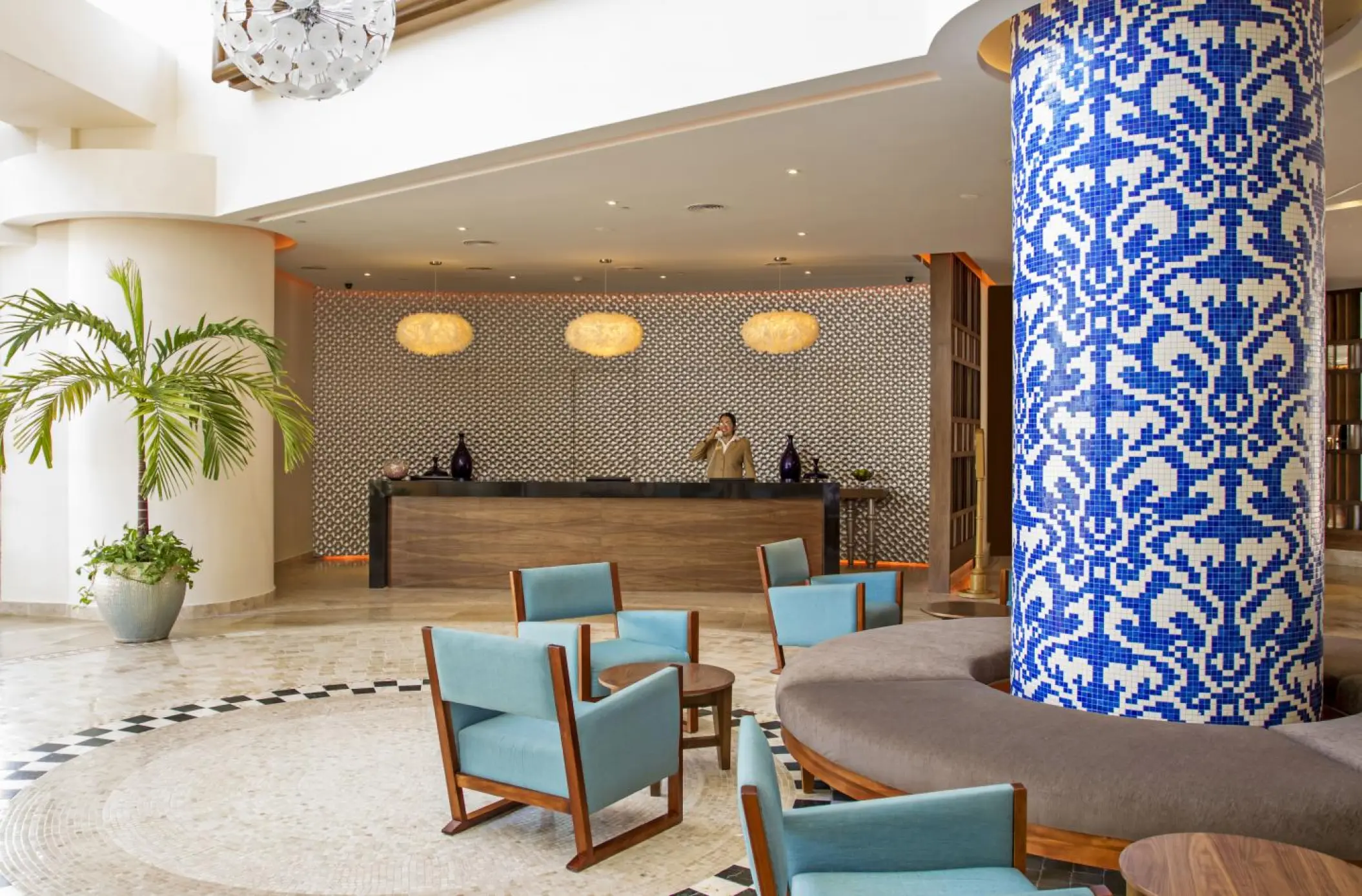 Sandos Cancun lobby with blue mosaic column, lounge seating, and wooden reception desk in Cancun