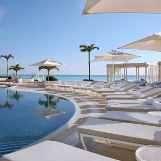 Tiered infinity pool with white sun loungers and umbrellas at Sandos Cancun, Cancun
