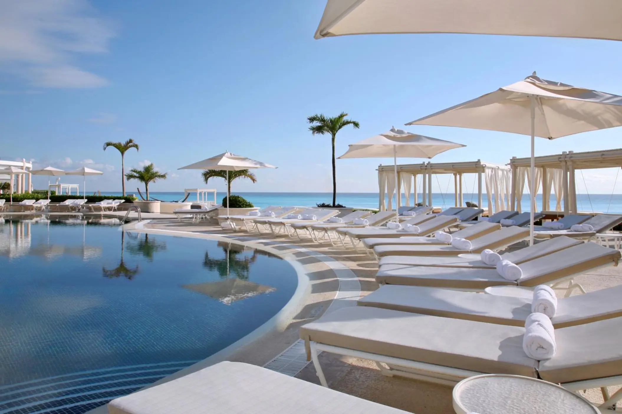 Tiered infinity pool with white sun loungers and umbrellas at Sandos Cancun, Cancun