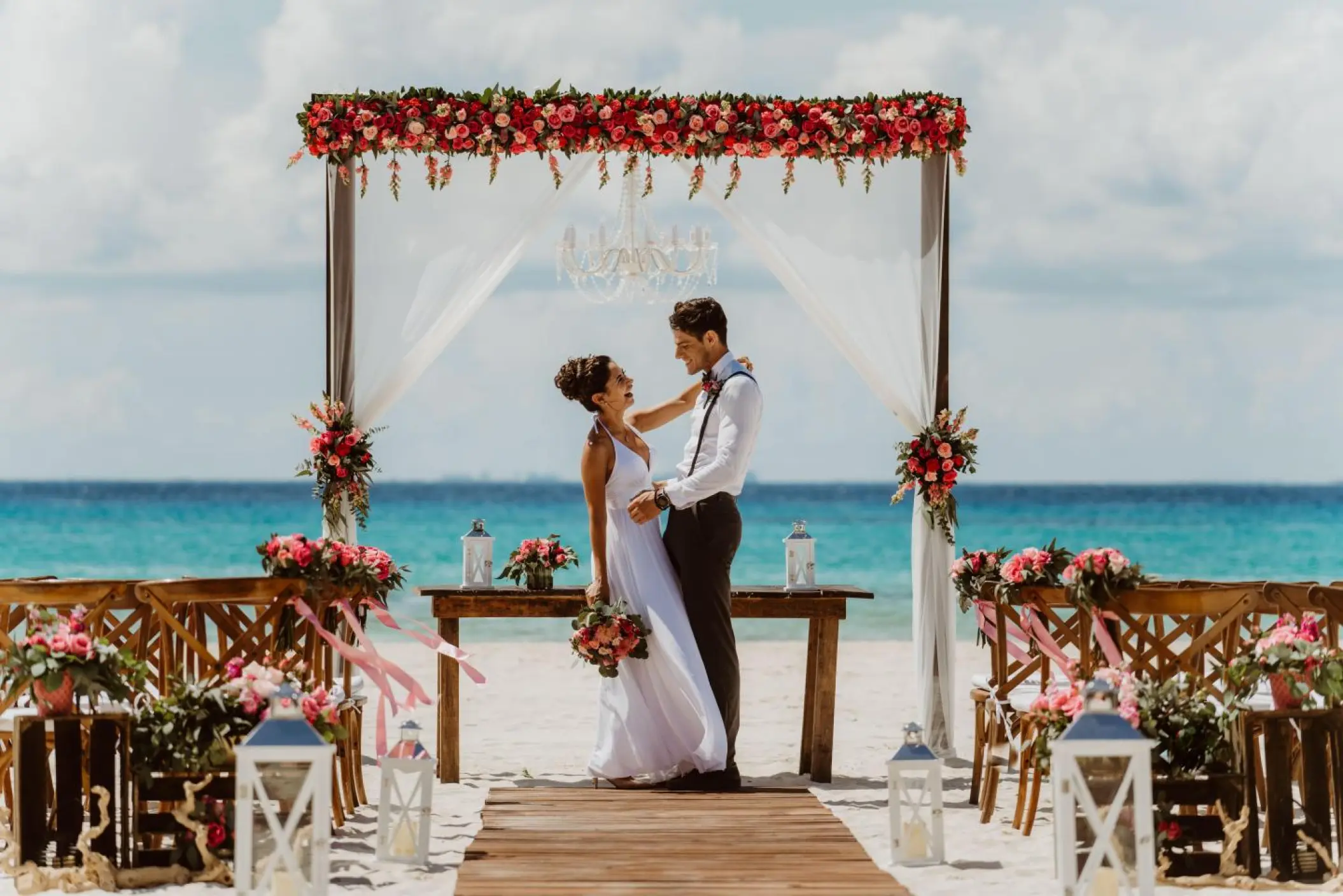 The bride and groom embracing under a floral arch at a Sandos Playacar beach ceremony, Playa Del Carmen