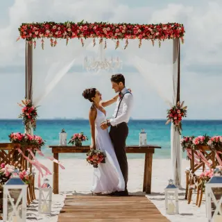 The bride and groom embracing under a floral arch at a Sandos Playacar beach ceremony, Playa Del Carmen