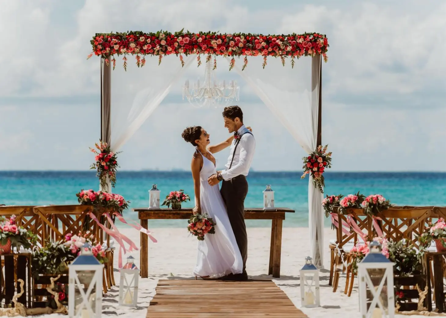 The bride and groom embracing under a floral arch at a Sandos Playacar beach ceremony, Playa Del Carmen