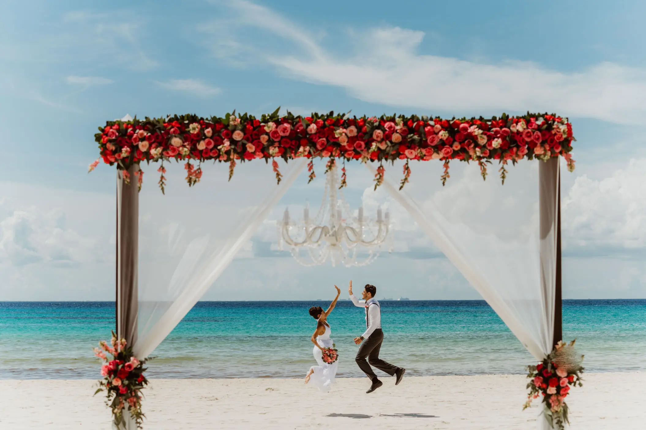 The bride and groom high-fiving under a floral beach ceremony arch at Sandos Playacar, Playa Del Carmen