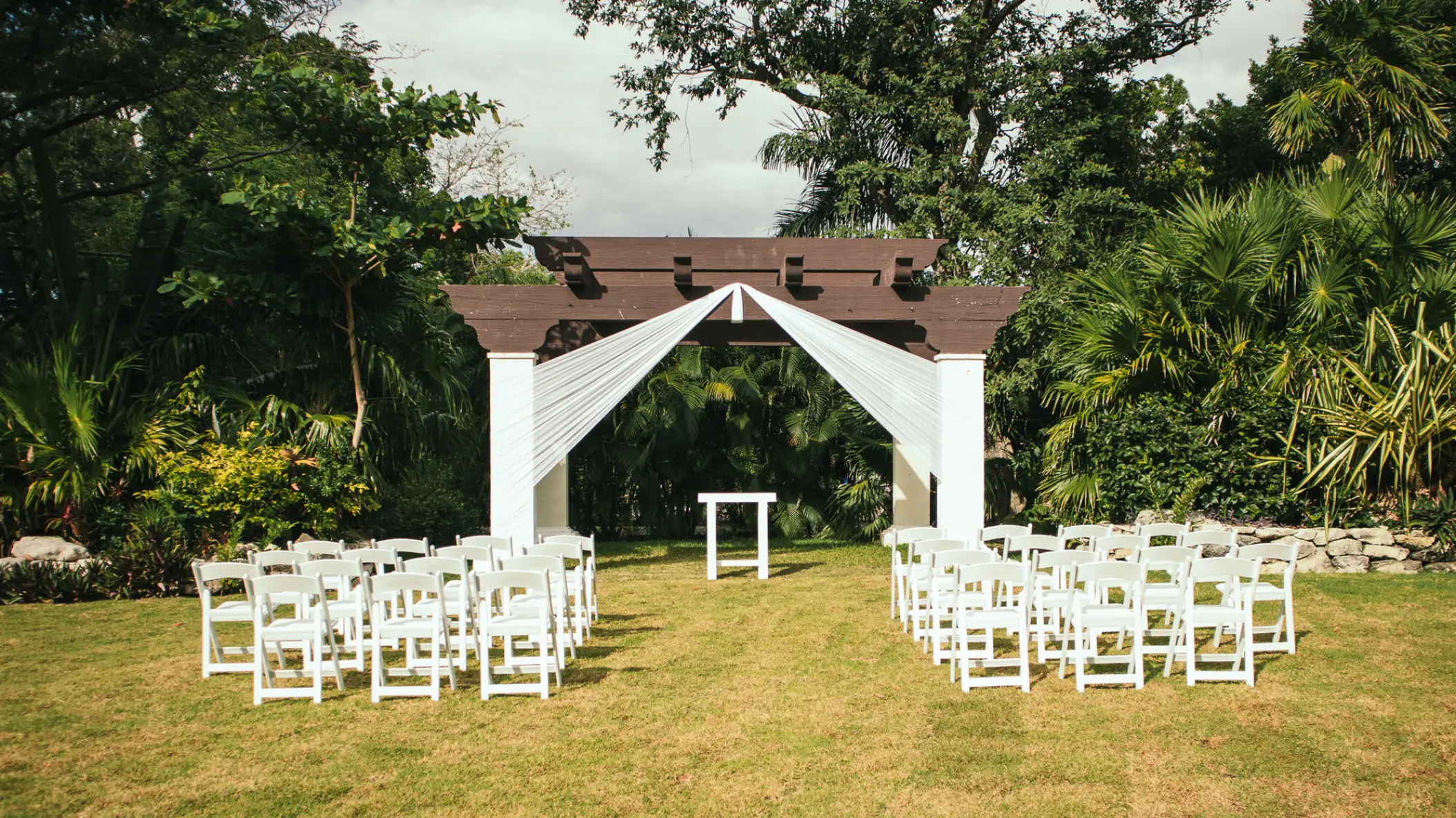 Garden wedding ceremony setup with white chairs and a wooden gazebo at Sandos Playacar, Playa Del Carmen