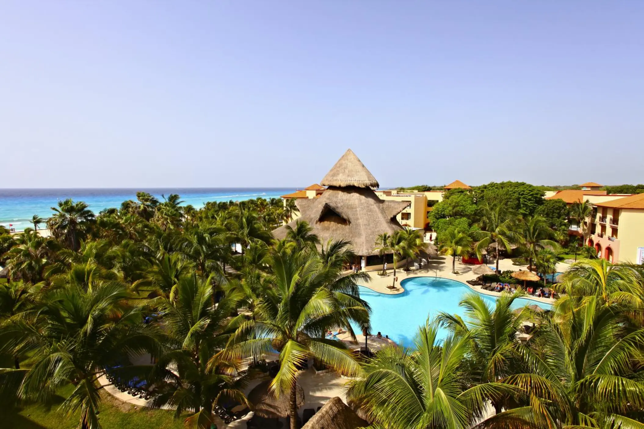 Sandos Playacar pool view surrounded by tropical palm trees and a thatched palapa, Playa Del Carmen