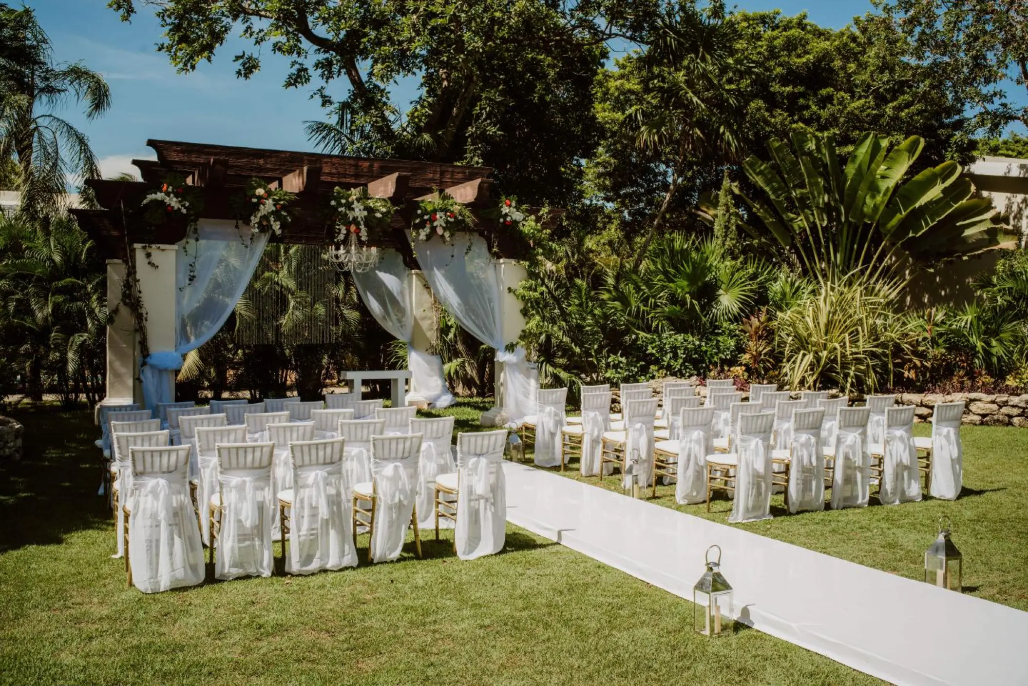 Garden wedding ceremony setup with a draped wooden pergola at Sandos Playacar, Playa Del Carmen