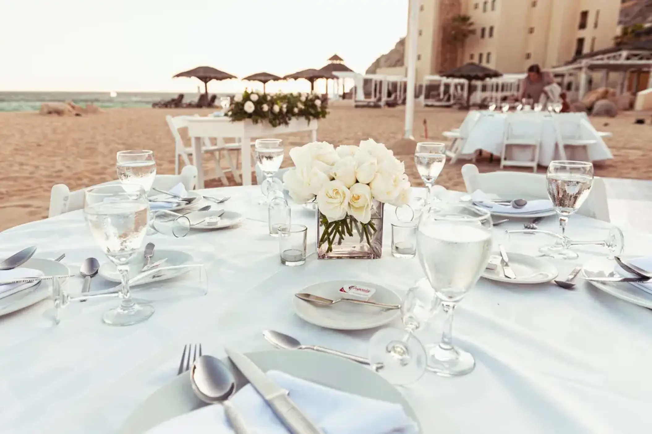 Beachfront wedding reception table with white roses and linens at Sandos Finisterra, Cabo San Lucas