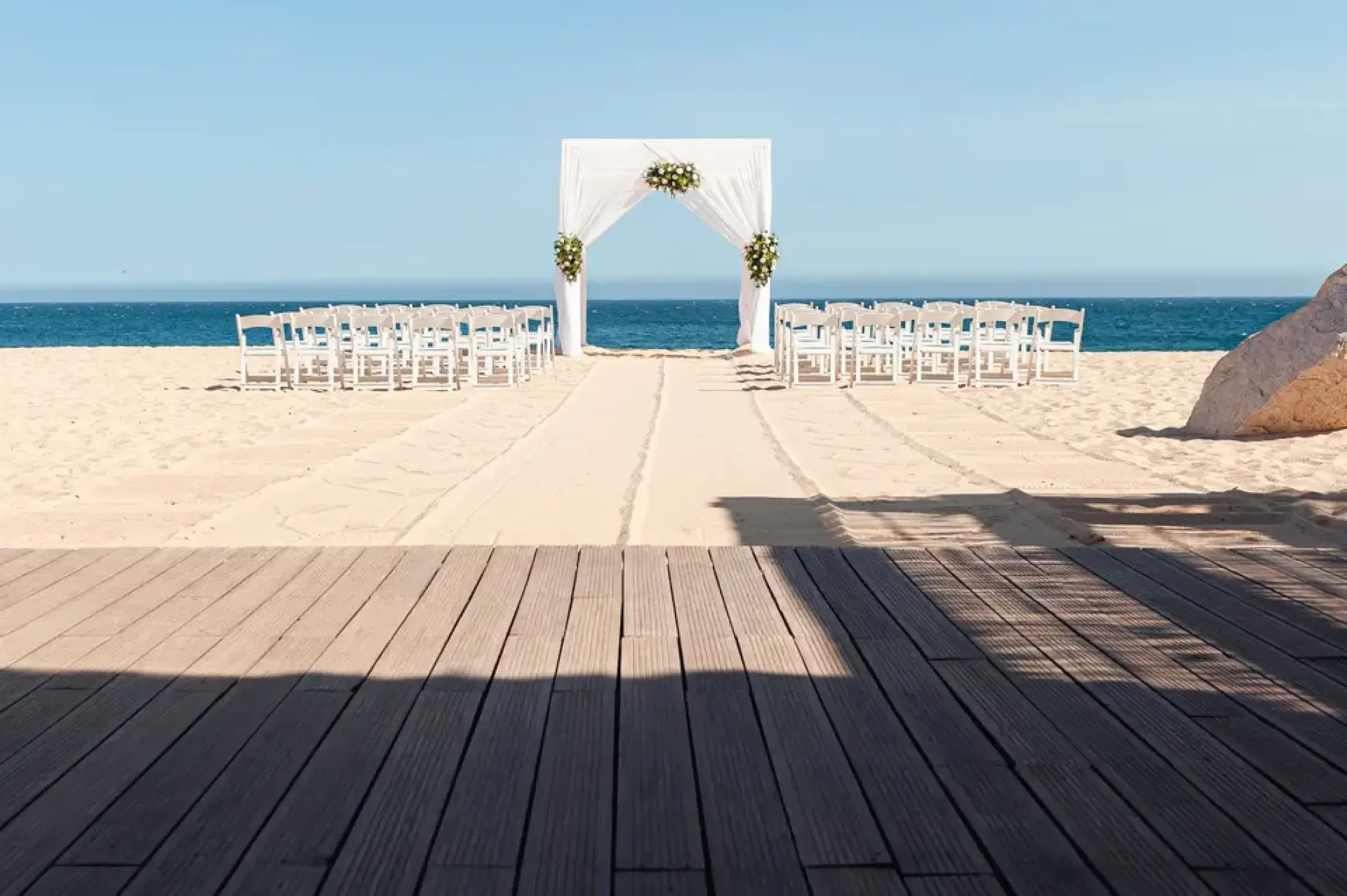 Beachfront wedding ceremony with white arch and chairs at Sandos Finisterra, Cabo San Lucas