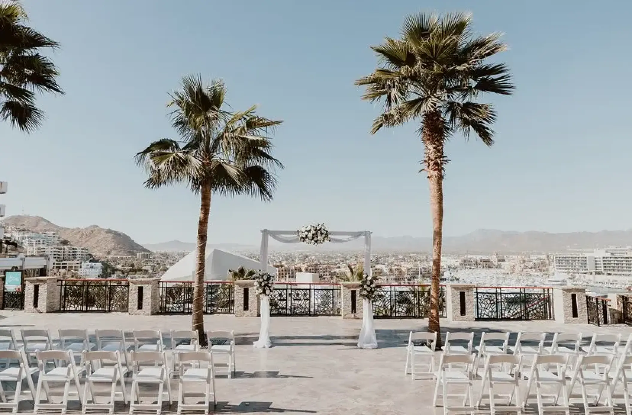Terrace wedding ceremony with white chairs and floral arch at Sandos Finisterra, Cabo San Lucas