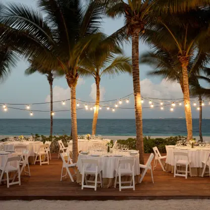 Beachfront wedding reception on a wooden deck with string lights and palm trees at Finest Playa Mujeres, Cancun