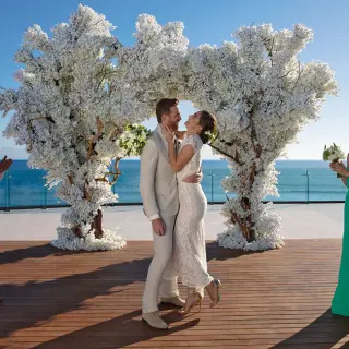 Wedding ceremony on a wooden deck with a white floral arch at Secrets Bahia Mita, Puerto Vallarta