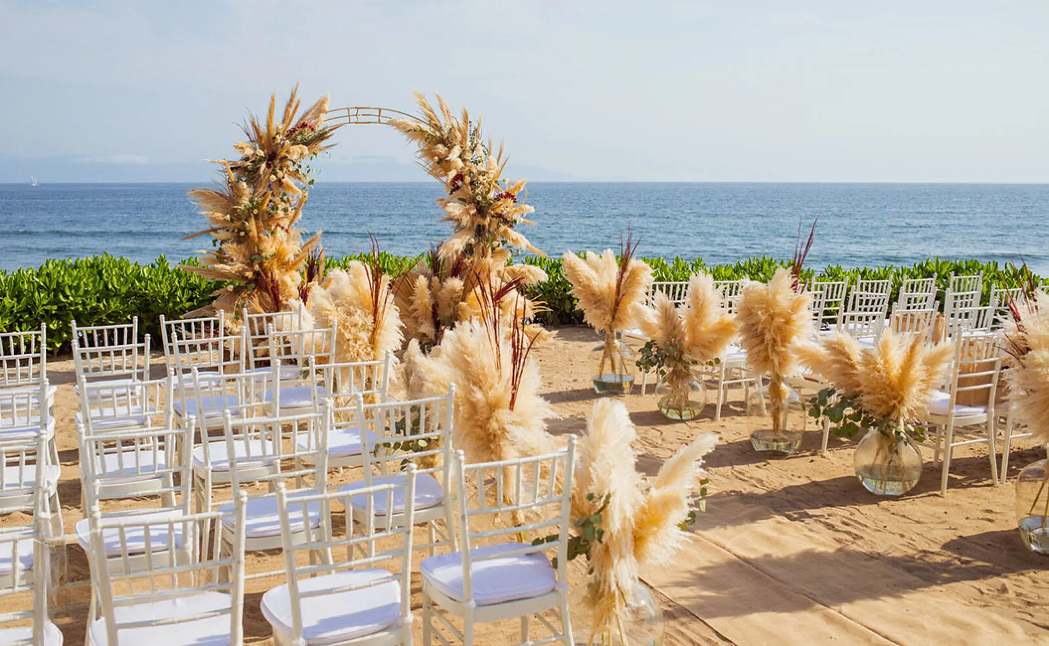 Beachfront wedding ceremony with pampas grass arch and white chairs at Secrets Bahia Mita, Puerto Vallarta