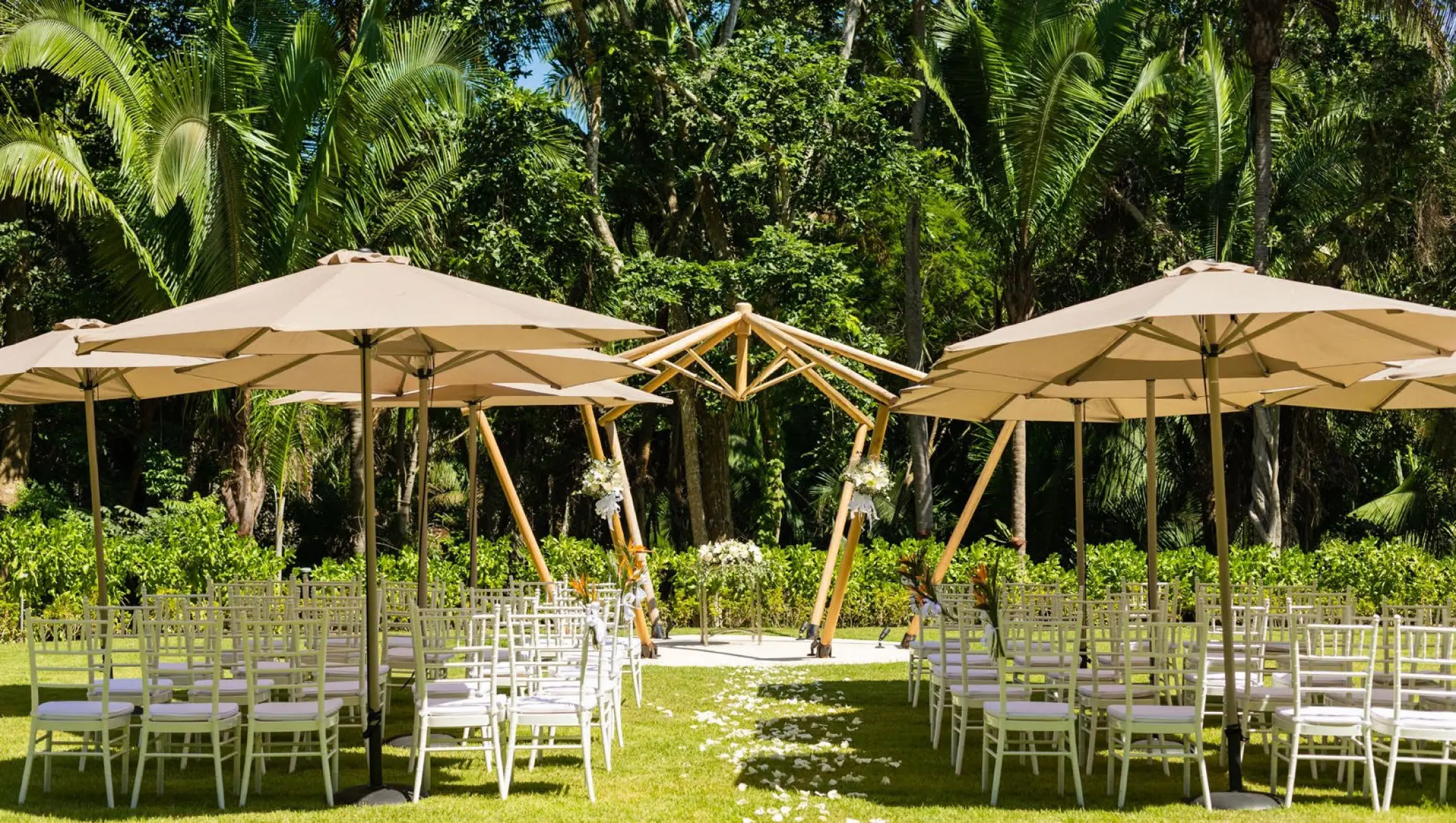 Garden wedding ceremony with a wooden arch and beige umbrellas at Secrets Bahia Mita, Puerto Vallarta