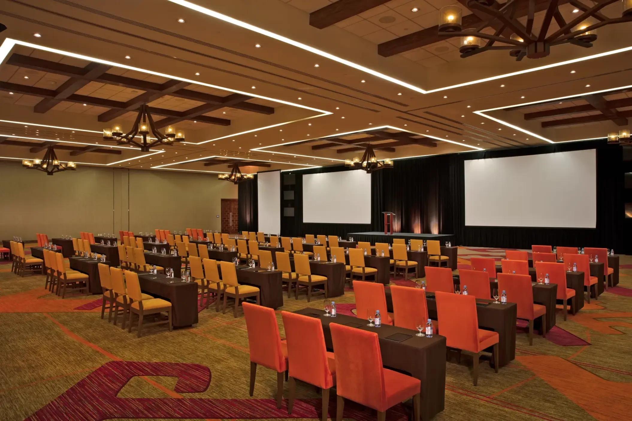 Ballroom set for a convention with rows of orange chairs and projection screens at Secrets Akumal, Riviera Maya