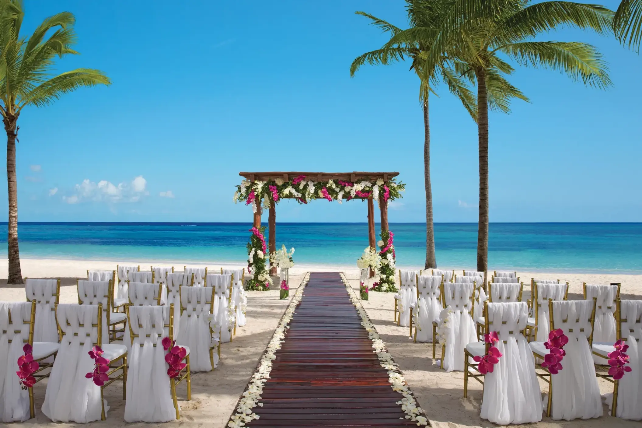 Beachfront wedding ceremony setup with floral arch and wooden aisle at Secrets Akumal, Riviera Maya