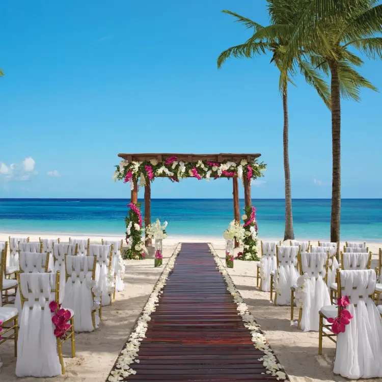 Beachfront wedding ceremony setup with floral arch and wooden aisle at Secrets Akumal, Riviera Maya