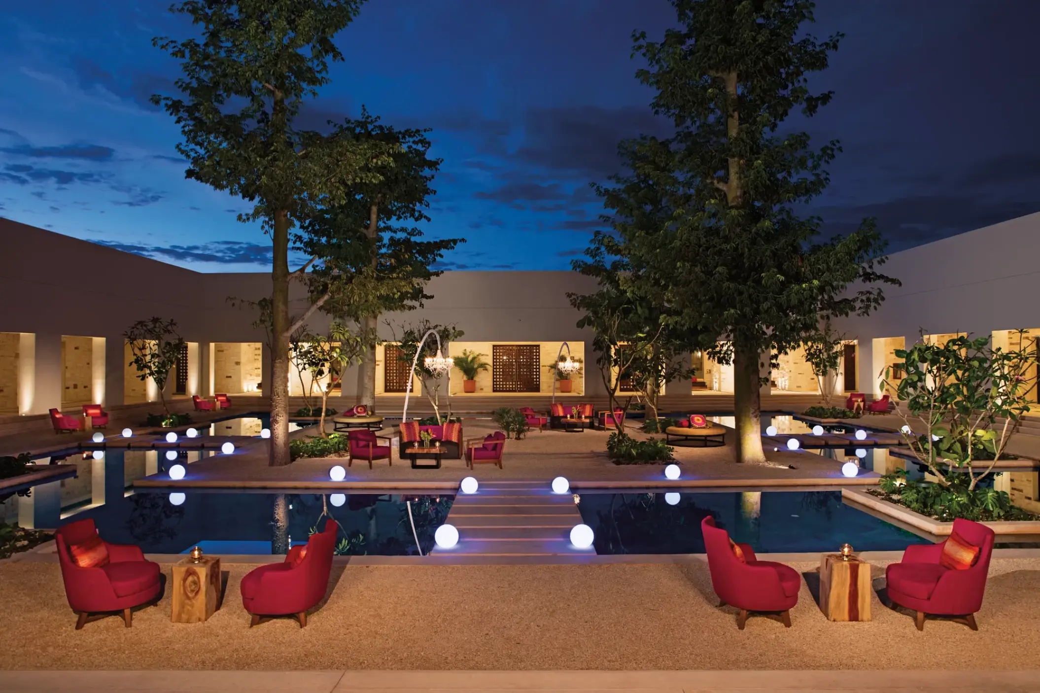 Secrets Akumal outdoor plaza with red lounge seating and glowing orb lights at night, Riviera Maya