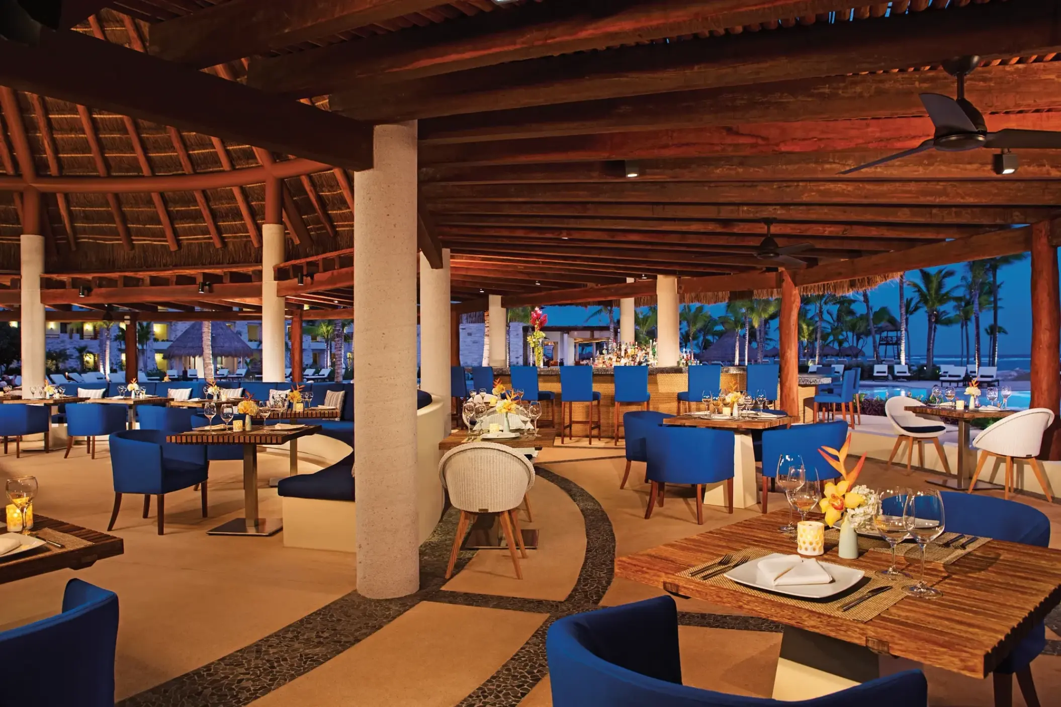 Seaside Grill restaurant with blue chairs and thatched roof at Secrets Akumal, Riviera Maya