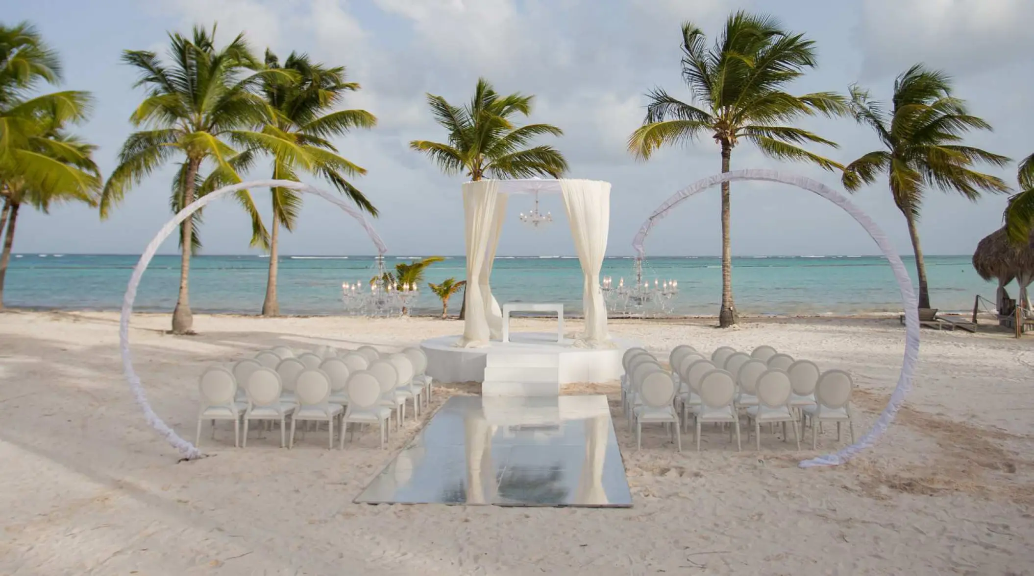 Juanillo Beach wedding ceremony setup with white floral arches and drapes at Secrets Cap Cana, Punta Cana