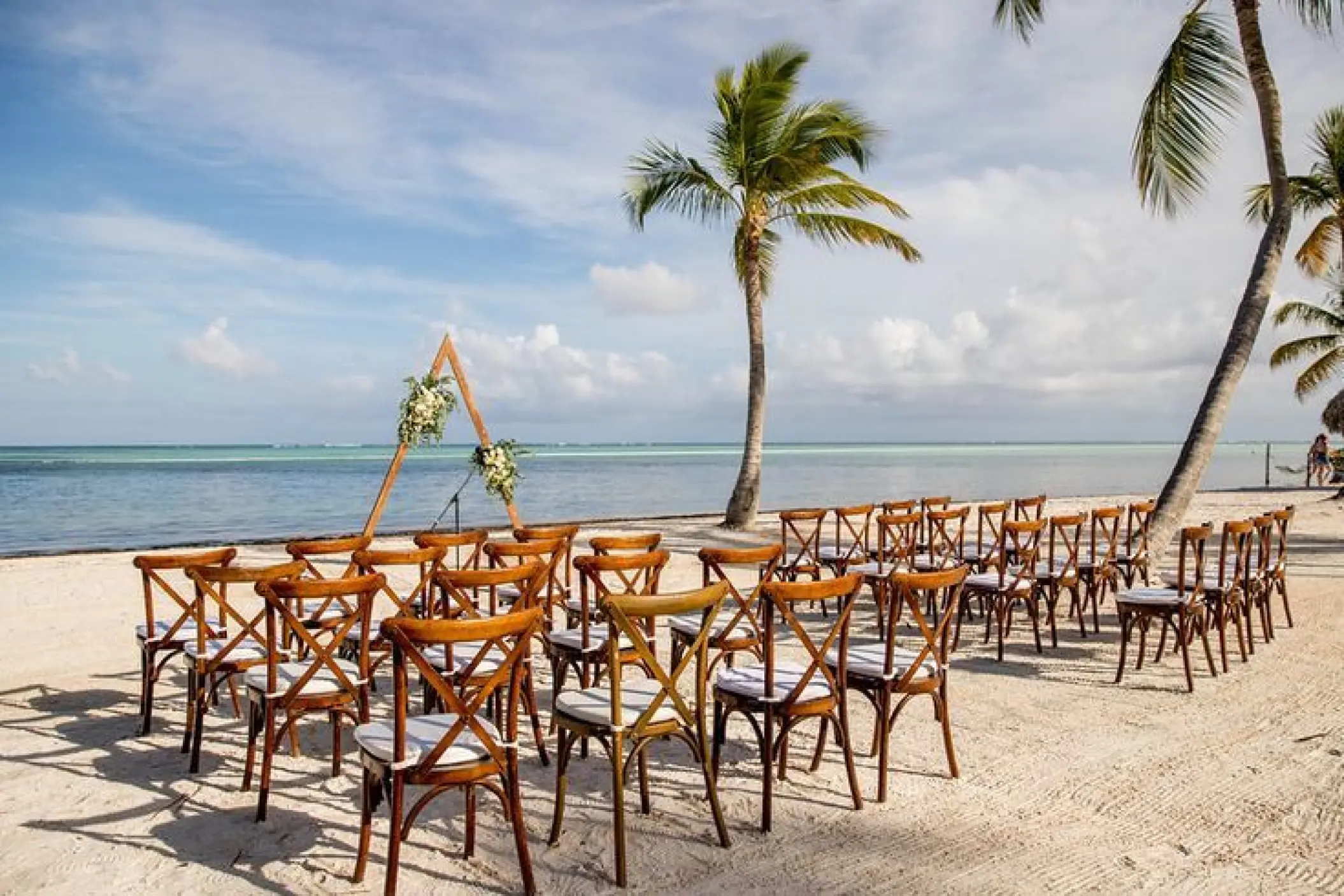 Beachfront wedding ceremony with wooden cross-back chairs and triangle arch at Secrets Cap Cana, Punta Cana