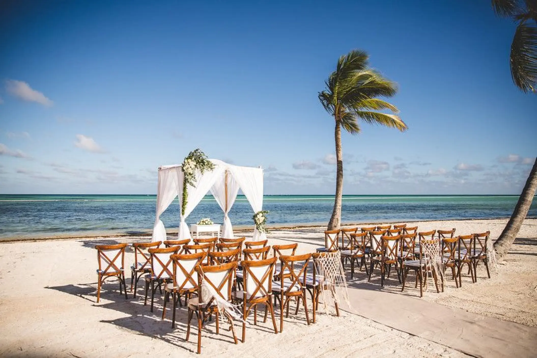 Beachfront wedding ceremony with white draped gazebo and wooden chairs at Secrets Cap Cana, Punta Cana