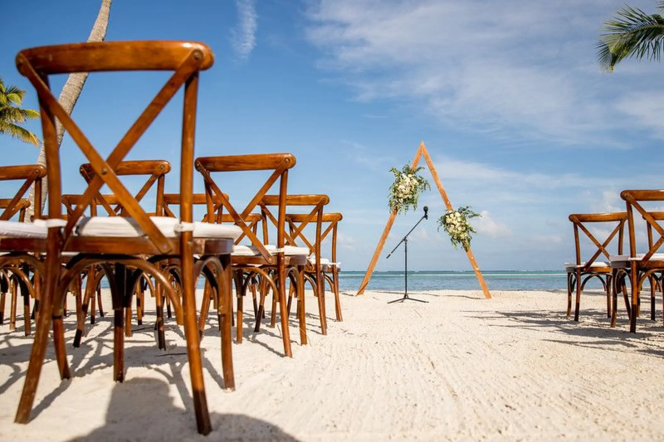 Beachfront wedding ceremony with a triangular wooden arch and cross-back chairs at Secrets Cap Cana, Punta Cana