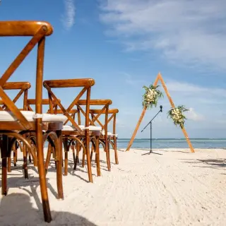 Beachfront wedding ceremony with a triangular wooden arch and cross-back chairs at Secrets Cap Cana, Punta Cana