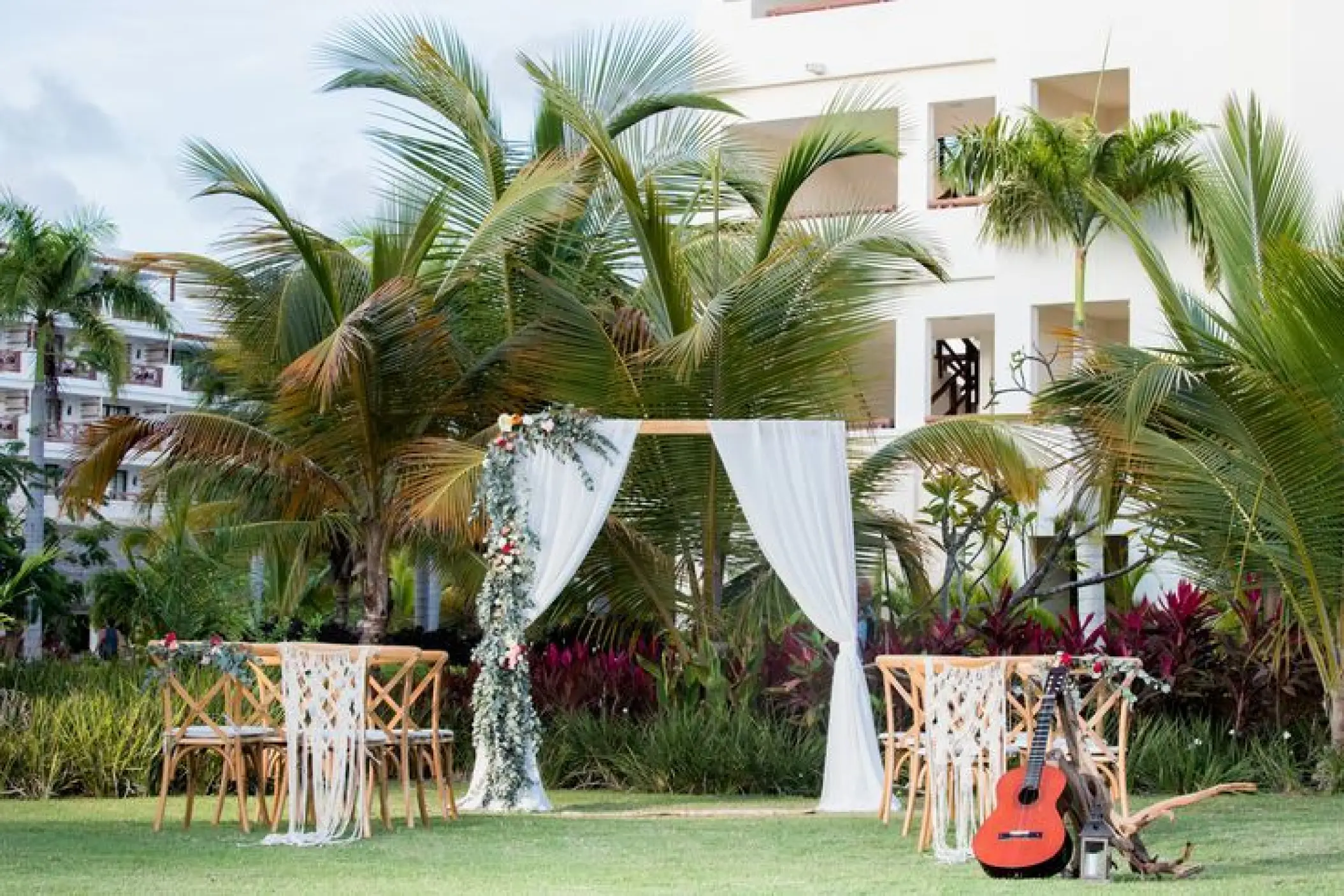 Garden wedding ceremony arch with white drapes and wooden chairs at Secrets Cap Cana, Punta Cana
