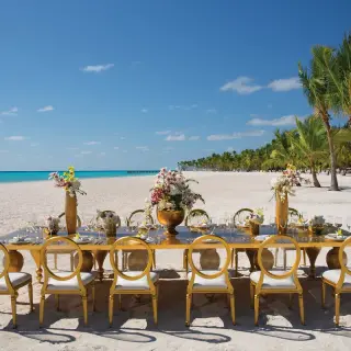 Long gold reception table with floral centerpieces on the beach at Secrets Cap Cana, Punta Cana