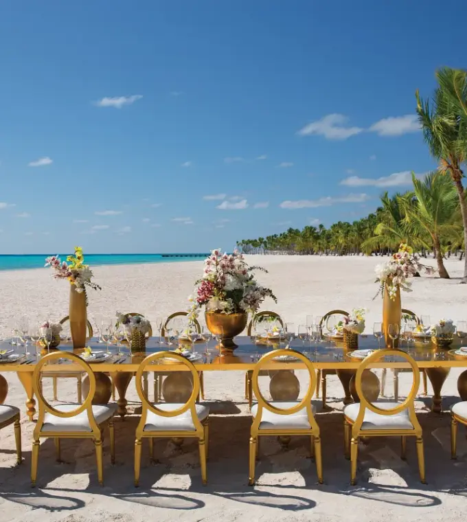 Long gold reception table with floral centerpieces on the beach at Secrets Cap Cana, Punta Cana