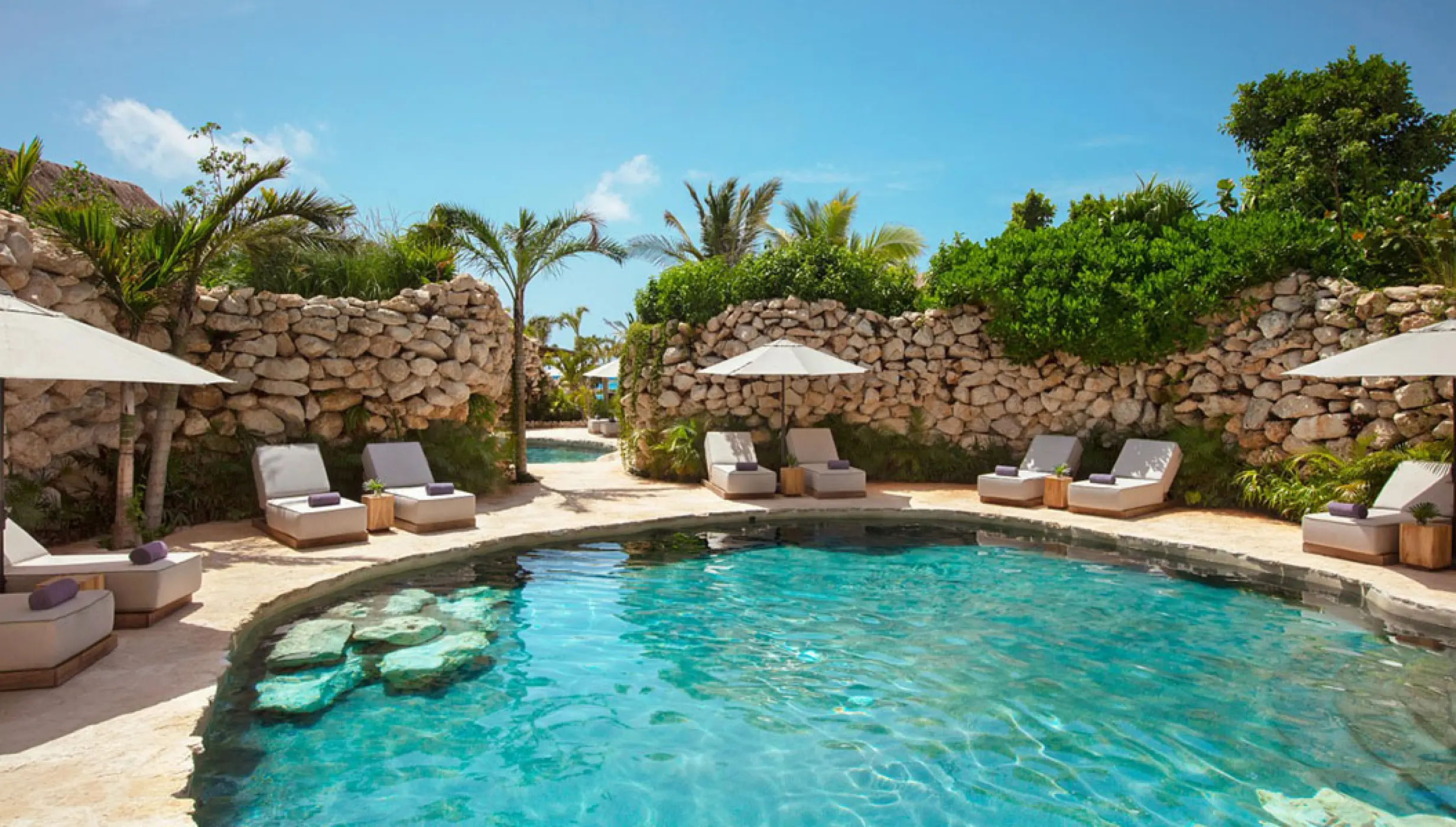 Cenote pool surrounded by stone walls and lounge chairs at Impression Moxché, Playa Del Carmen