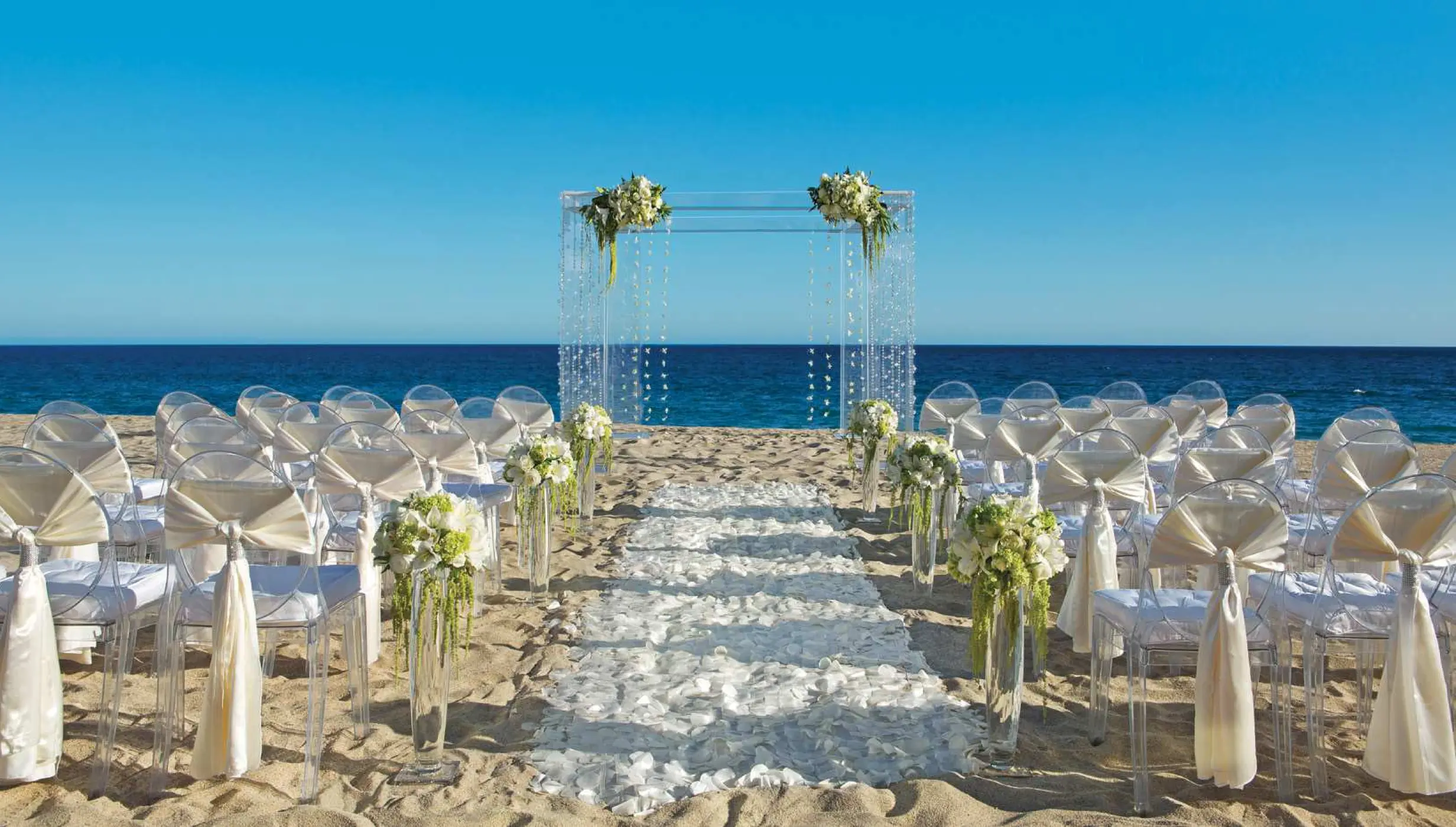 Beachfront wedding ceremony with an acrylic arch and petal aisle at Secrets Puerto Los Cabos, Cabo San Lucas
