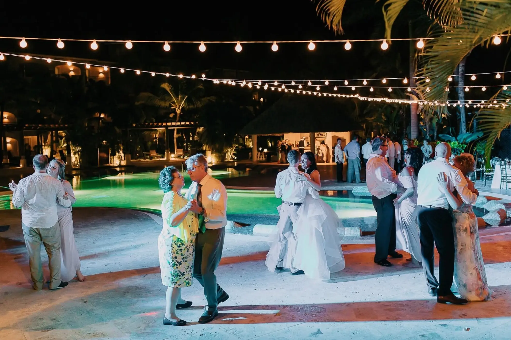 Wedding reception guests dancing under string lights by the pool at Secrets Royal Beach, Punta Cana