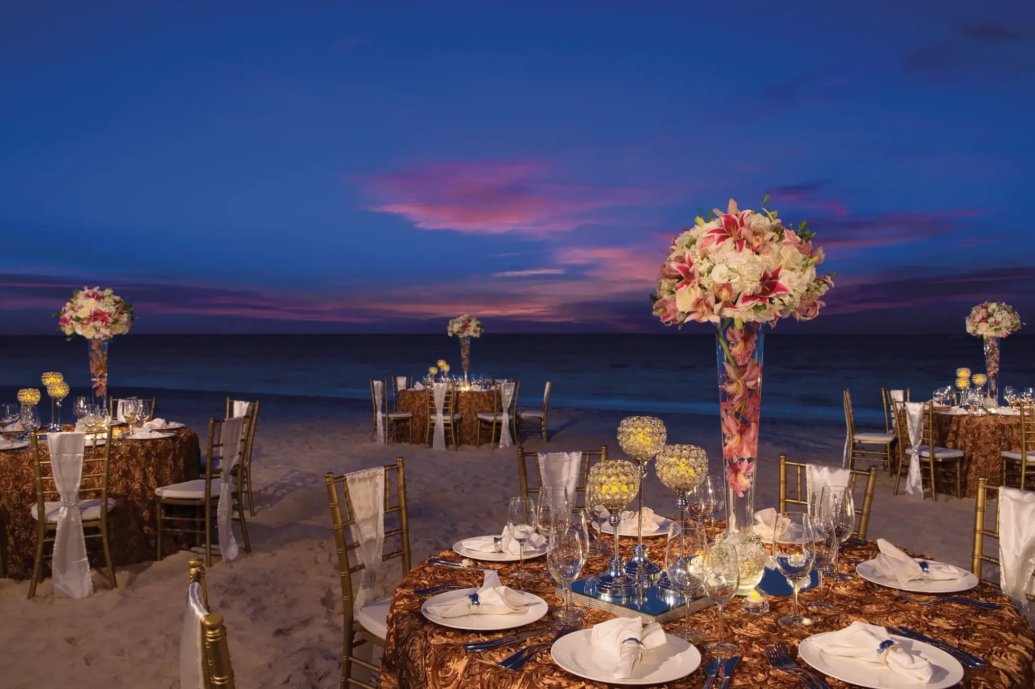 Beachfront wedding reception at sunset with floral centerpieces at Secrets Royal Beach, Punta Cana