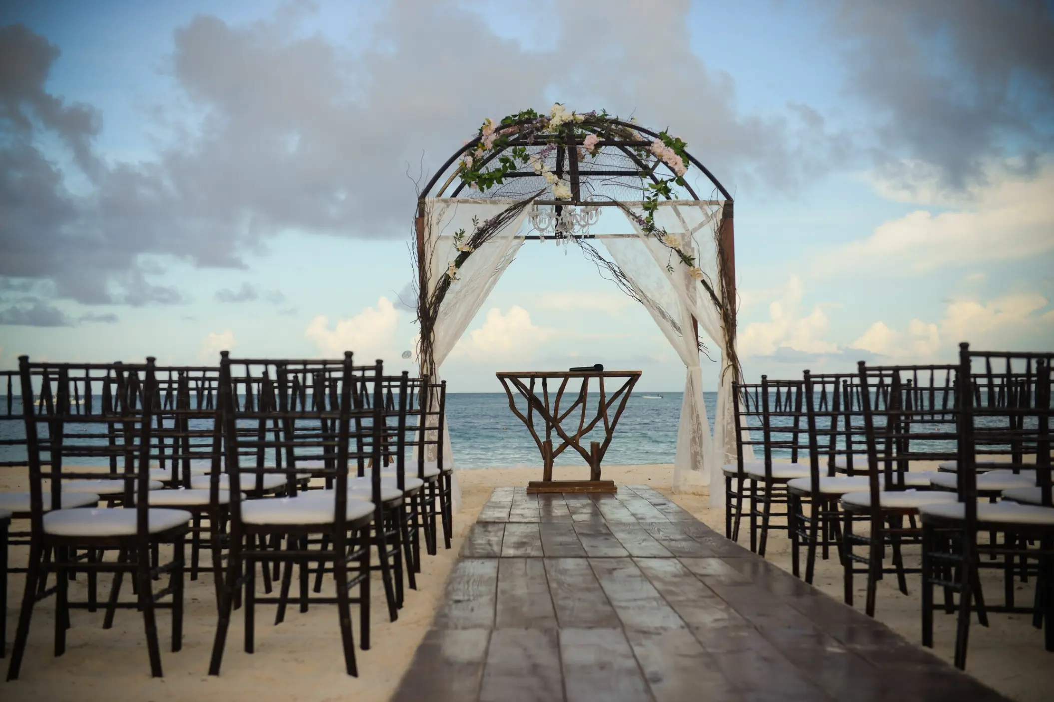 Beachfront wedding ceremony setup with a floral arch and wooden aisle at Secrets Royal Beach, Punta Cana