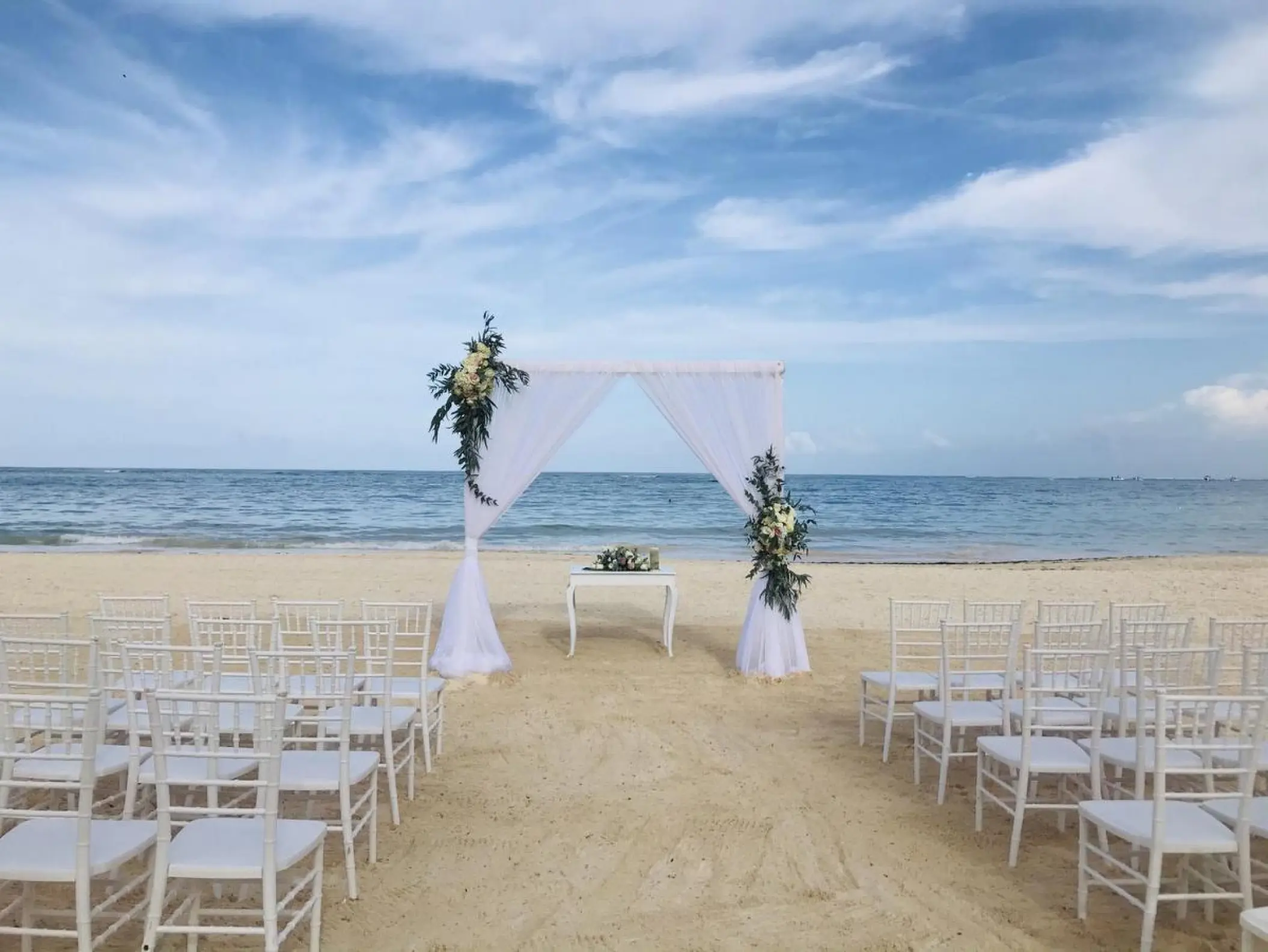Beachfront wedding ceremony with white draped arch and chairs at Secrets Royal Beach, Punta Cana