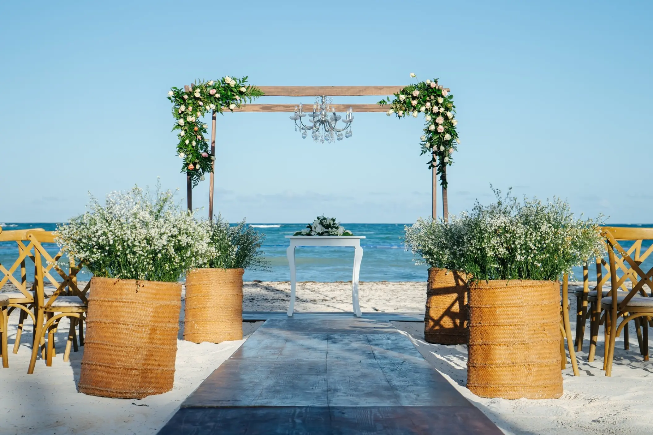 Beachfront wedding ceremony with a floral wooden arch and chandelier at Secrets Royal Beach, Punta Cana