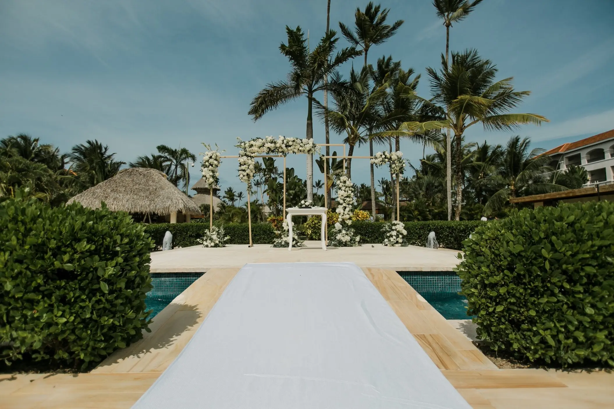 White floral arch wedding ceremony setup by the pool at Secrets Royal Beach, Punta Cana