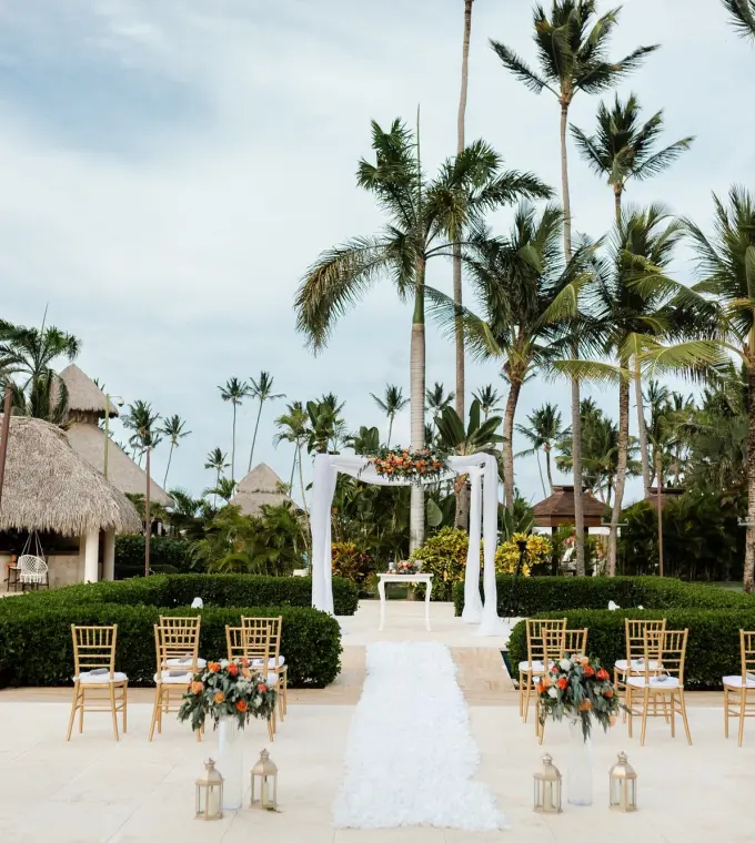 Outdoor wedding ceremony setup with white floral arch and gold chairs at Secrets Royal Beach, Punta Cana