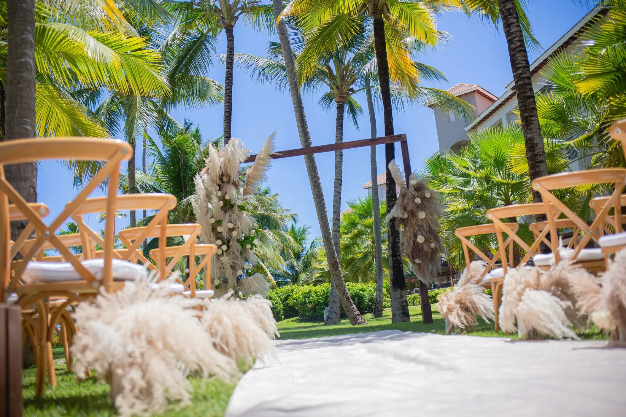 Garden wedding ceremony aisle with wooden chairs and pampas grass at Secrets Royal Beach, Punta Cana