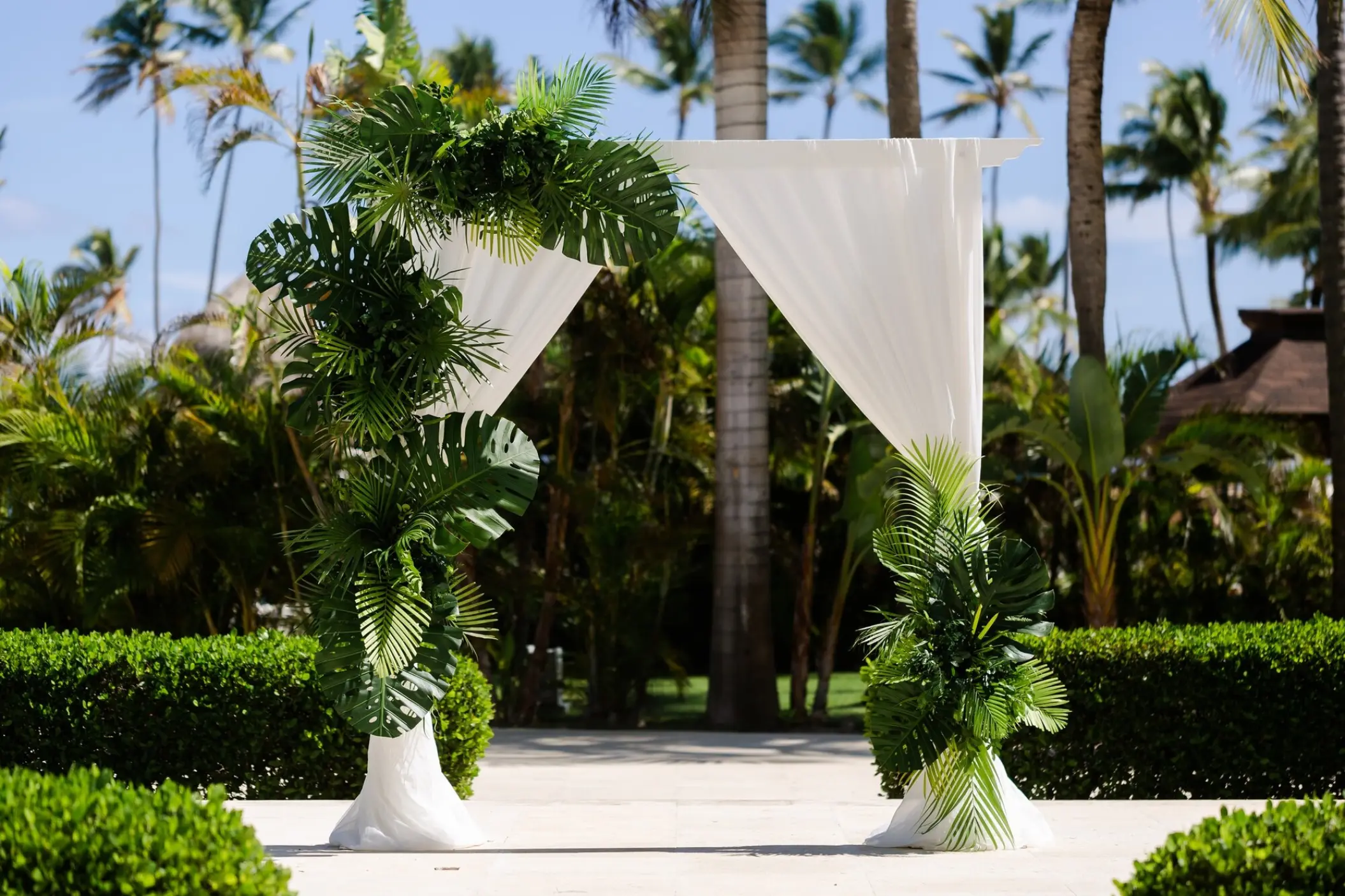 Tropical wedding ceremony arch with white fabric and monstera leaves at Secrets Royal Beach, Punta Cana