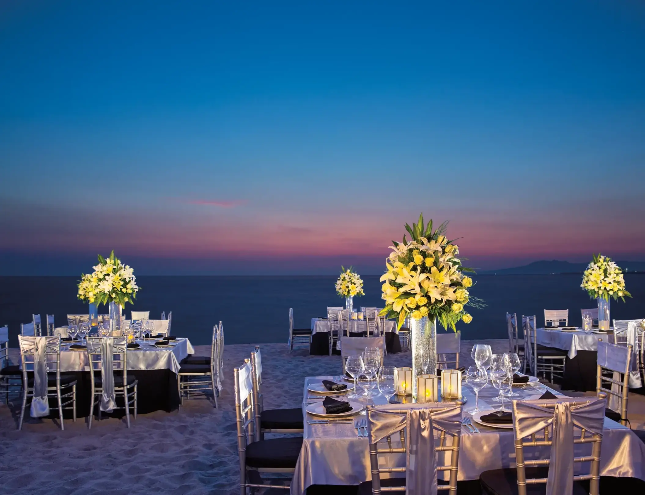 Beachfront wedding reception tables with floral centerpieces at sunset at Secrets Vallarta Bay, Puerto Vallarta