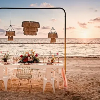 Beachfront wedding reception setup with hanging lanterns at Sensira Riviera Maya at sunset