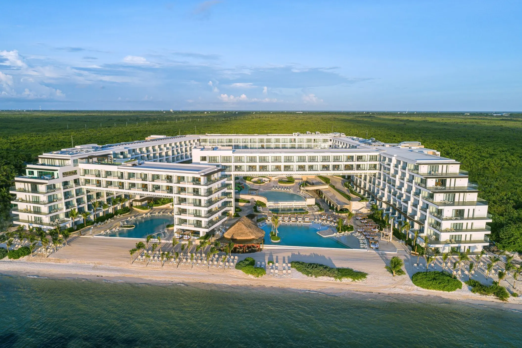 Aerial view of Sensira Riviera Maya beachfront buildings and pools surrounded by lush greenery