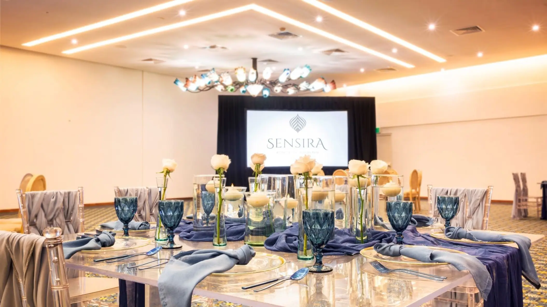 Indoor wedding reception at Sensira Riviera Maya with blue glassware and white rose centerpieces