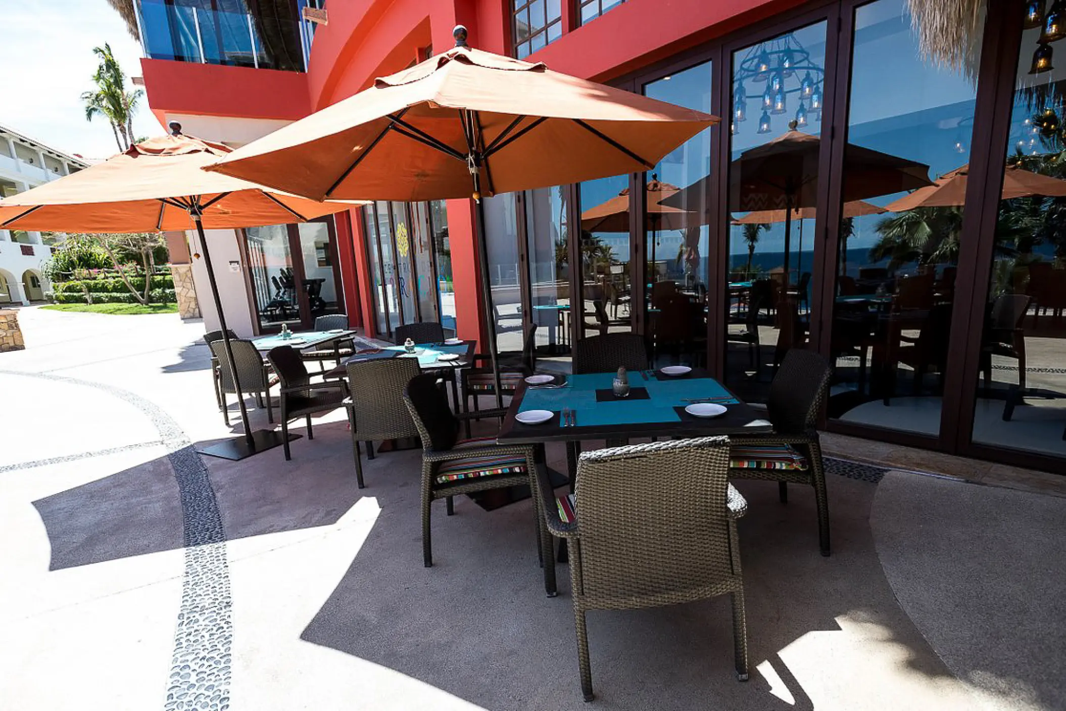 Outdoor patio dining with orange umbrellas and woven chairs at Hyatt Sirena del Mar, Cabo San Lucas