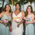 Bride Allison posing with her bridesmaids holding pink floral bouquets in front of palm trees