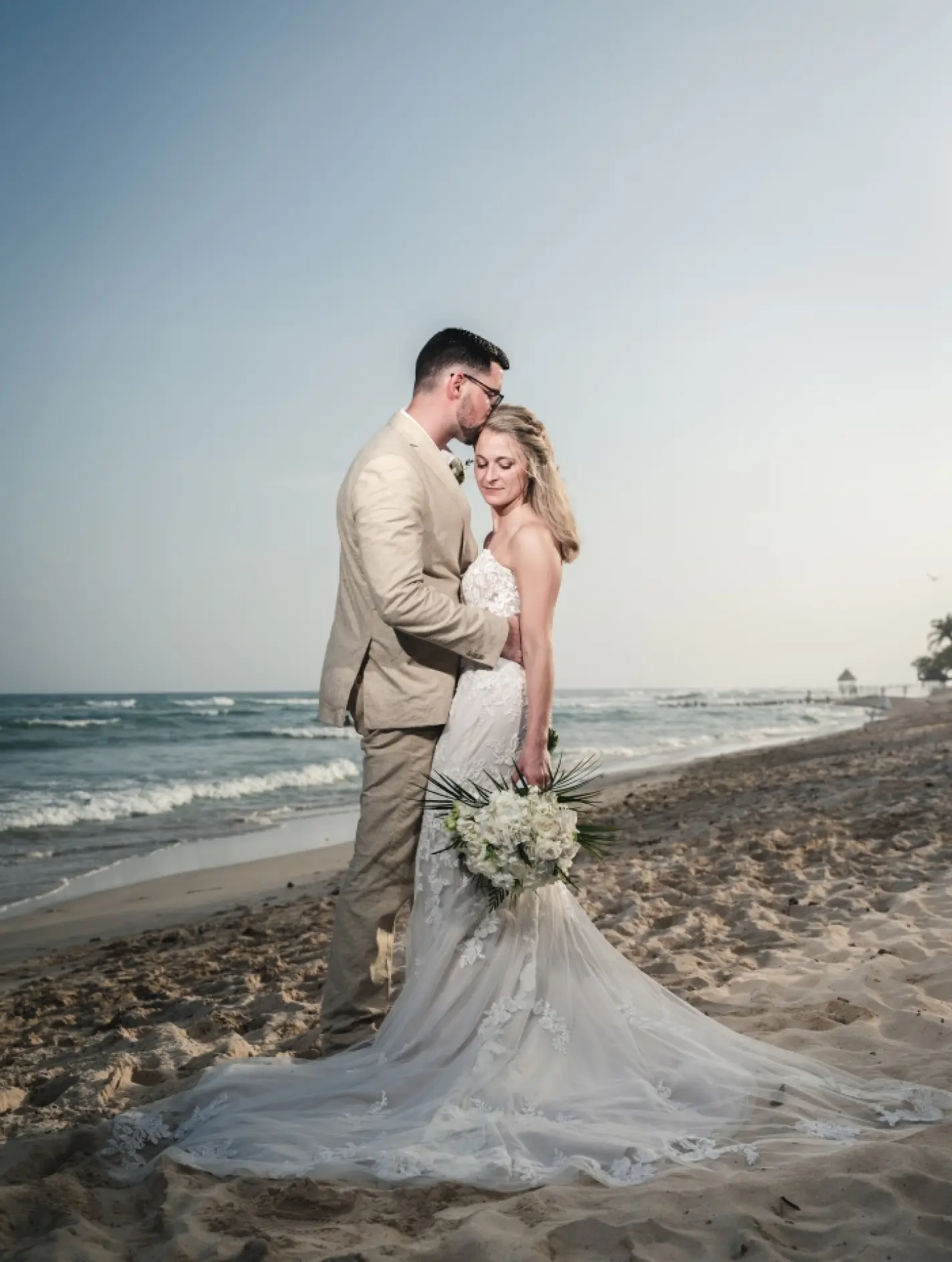 Danielle & Derrek's beach portrait with the groom kissing the bride's forehead
