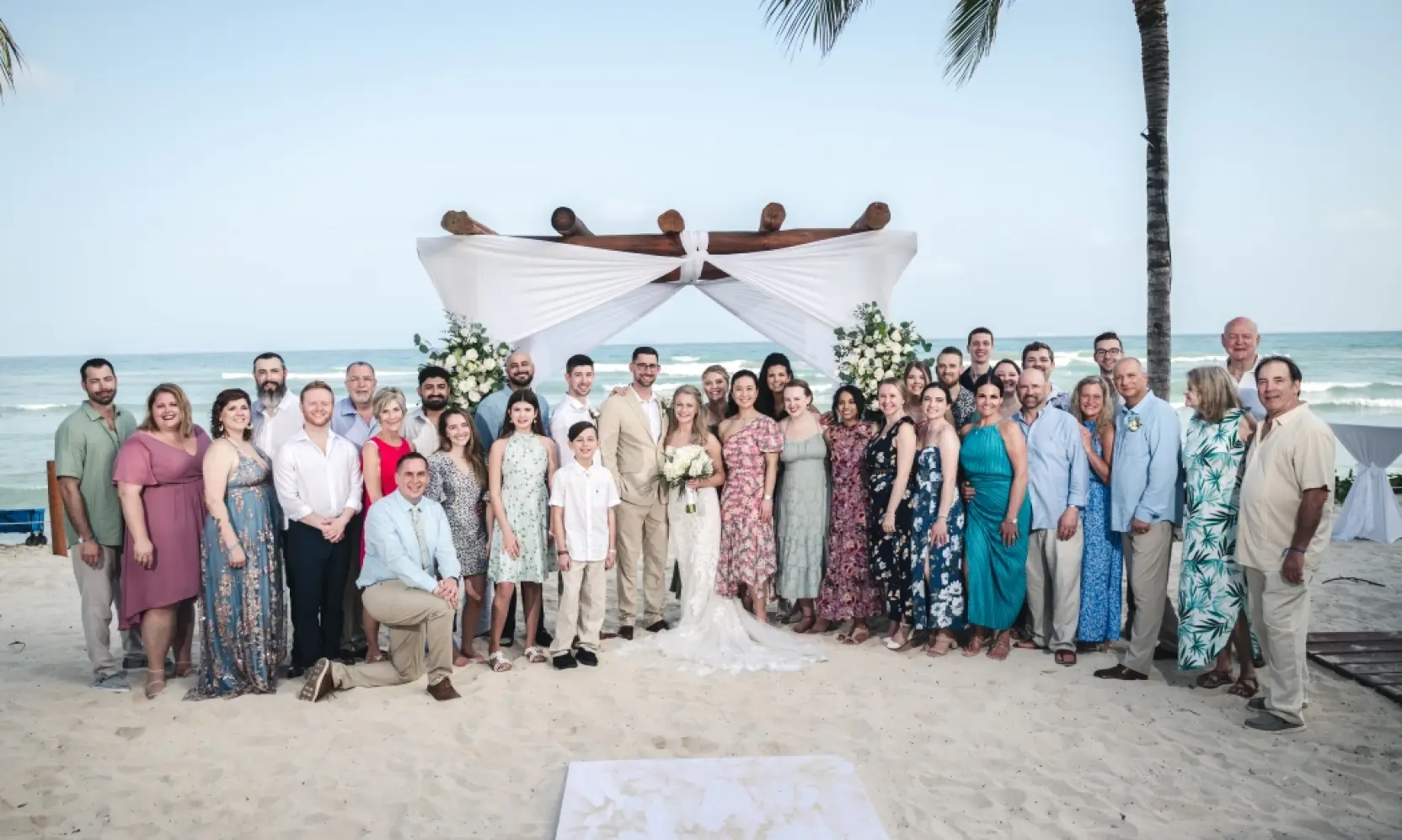 Danielle & Derrek posing with guests under a beach ceremony arch