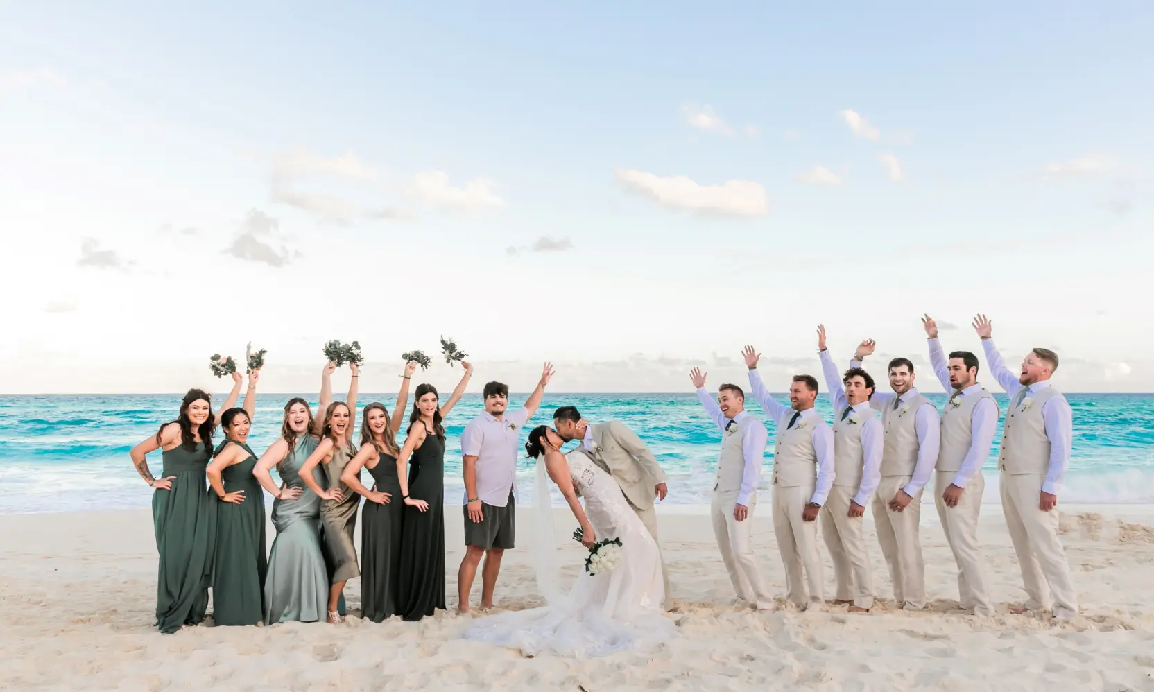 Danielle & Junya kissing on the beach with their wedding party at Paradisus Cancun